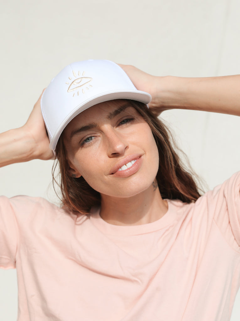 White and sand-colored trucker hat featuring The Mindry logo on the front. Worn by model facing forward.