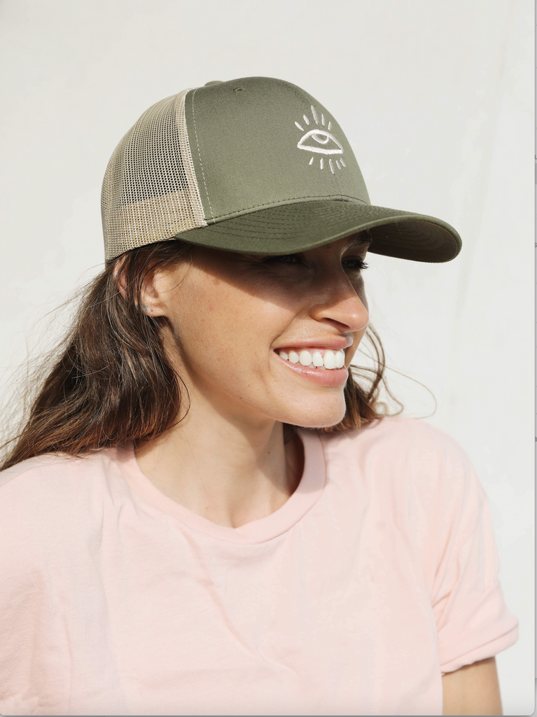 Green and tan trucker hat featuring The Mindry logo on the front. Worn by model looking to the right. 